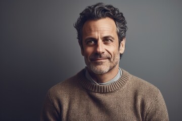 Obraz premium Portrait of a handsome mature man in sweater looking at camera and smiling while standing against grey background