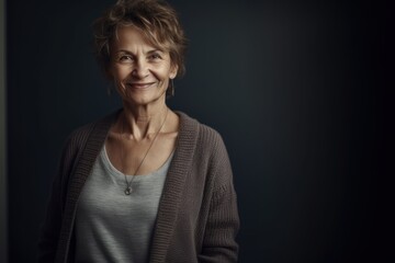 Portrait of a smiling senior woman standing against a dark background.