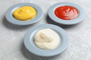 Plates with ketchup, mayonnaise and mustard on grey grunge table