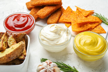 Bowls of different sauces, snacks and rosemary on white grunge table