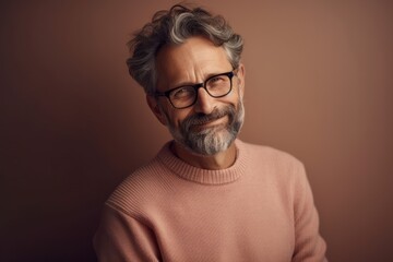 Portrait of handsome senior man with grey hair wearing glasses looking at camera and smiling while standing against brown background