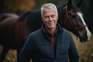Portrait of a handsome mature man with a horse in the autumn forest