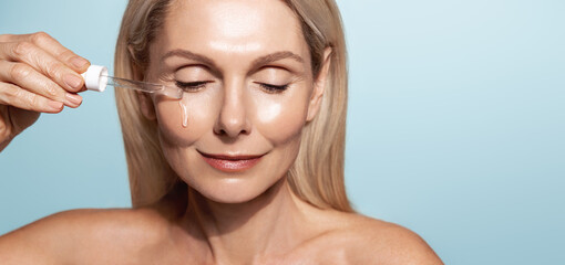 Spa and wellbeing. Middle aged woman applies lifting serum with dropper, uses cosmetic for senior...