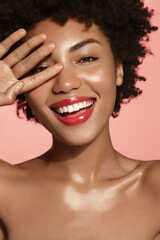 Vertical shot of gorgeous Black woman with healthy smile, touches her face and looks happy, has...