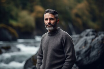 Portrait of a bearded man in a sweater against the background of a waterfall