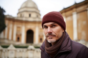 Portrait of a handsome middle-aged man in a hat, scarf and coat standing in front of the Pantheon in Rome, Italy