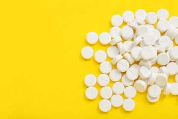 Heap of white pills on yellow background