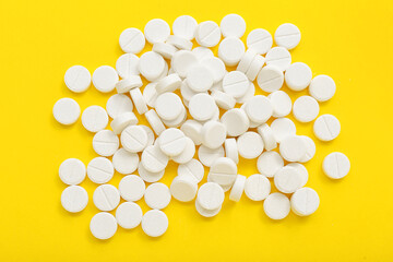 Heap of white pills on yellow background