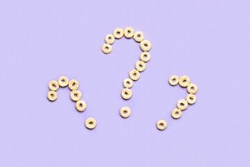 Question marks made of cereal rings on lilac background