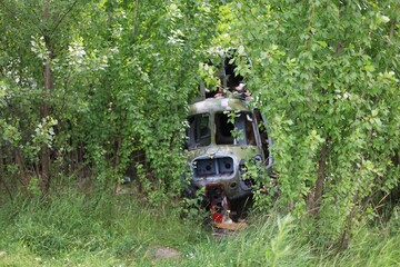 the abandoned ruins of a helicopter surrounded by green bushes and grass. Abandoned helicopter, abandoned plane