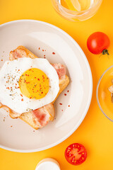 Delicious sandwich with fried egg and bacon on yellow background