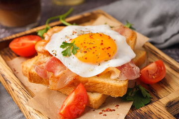 Delicious sandwich with fried egg, tomatoes and bacon on grunge grey background