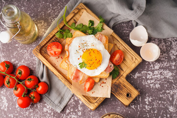 Delicious sandwich with fried egg, tomatoes and bacon on grunge grey background