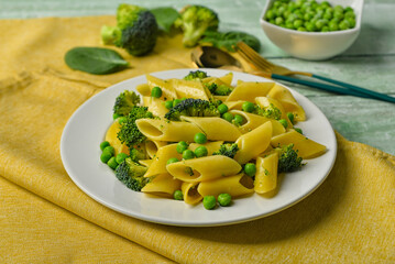 Plate with tasty penne pasta and broccoli on green wooden  background
