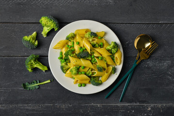 Plate with tasty penne pasta and broccoli on dark wooden background