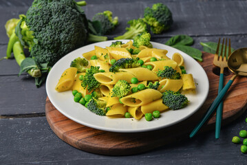 Plate with tasty penne pasta and broccoli on dark wooden background