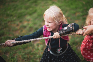 childhood, vacation and people concept - Little girl dressed as a pirate playing tug of war in...