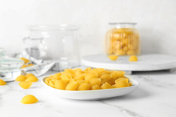Plate with raw conchiglie pasta on light background