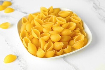 Plate with raw conchiglie pasta on white marble background