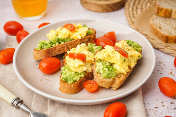 Plate with tasty scrambled eggs sandwiches and vegetables on light background