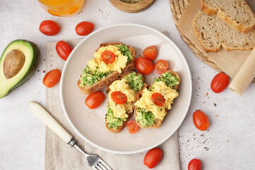 Plate with tasty scrambled eggs sandwiches and vegetables on light background