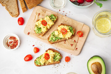 Wooden board with tasty scrambled eggs sandwich and vegetables on light background
