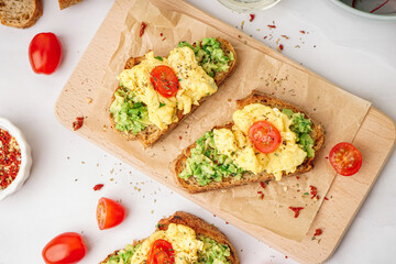 Wooden board with tasty scrambled eggs sandwich and vegetables on light background