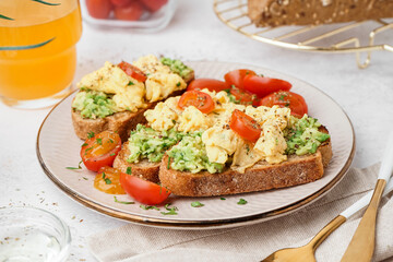 Plate with tasty scrambled eggs sandwich and vegetables on light background