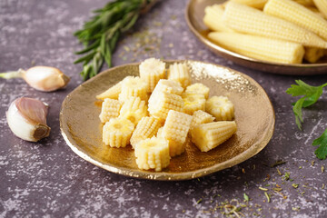Plate with cut canned baby corn cobs on grey grunge background