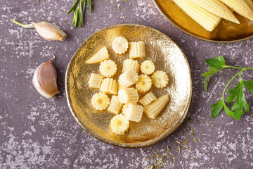 Plate with cut canned baby corn cobs on grey grunge background