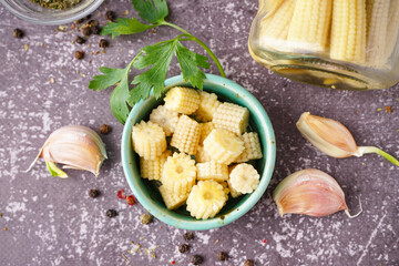 Bowl with cut canned baby corn cobs on grey grunge background