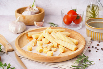 Plate with cut and whole canned baby corn cobs on light background