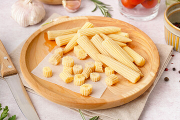 Plate with cut and whole canned baby corn cobs on light background
