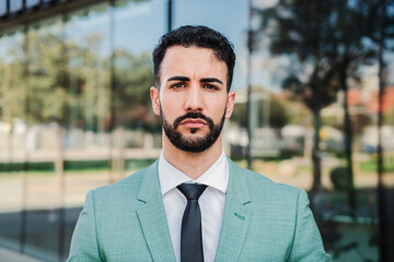 Close up portrait of serious business man with suit and tie standing at workspace looking at camera. Front view of focused handsome corporate executive employee with ambitious and successful attitude