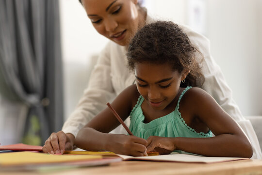 Smiling biracial mother sitting at dining table helping her daughter with school work