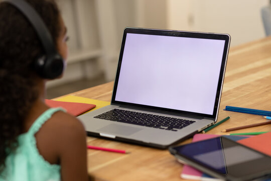 Focused biracial girl wearing headphones and learning at home using laptop, copy space on screen