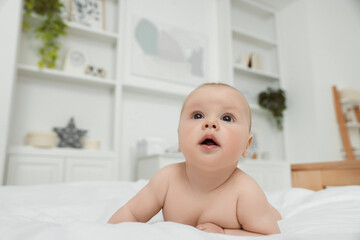 Cute baby lying on white bed at home, space for text