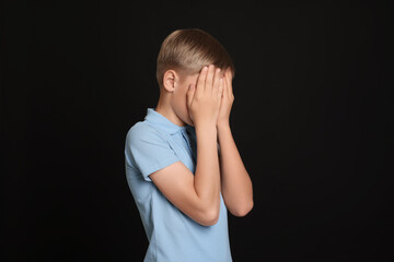 Boy covering face with hands on black background. Children's bullying