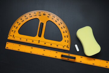 Ruler, protractor, chalk and sponge on black table, flat lay