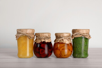 Jars with preserved fruit jams on white wooden table