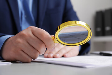 Man looking at document through magnifier at white table, closeup. Searching concept