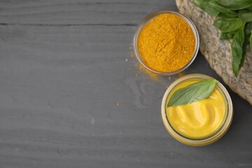 Tasty curry sauce, powder and basil leaves on grey wooden table, flat lay. Space for text