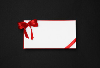 Blank gift card with red bow on black background, top view
