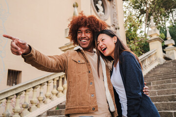 Young multiracial couple walking and having fun on a romantic trip pointing monument. African american boyfriend and chinese girlfriend smiling bonding together sightseeing with affectionate attitude