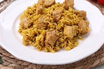 Plate of delicious rice with chicken on wicker mat, closeup