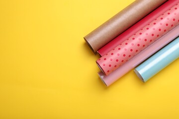 Rolls of colorful wrapping papers on yellow background, top view. Space for text