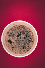 Cold cola in the plactic cup on the red background.