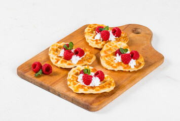 Waffles with cream and raspberries on a wooden board. White background