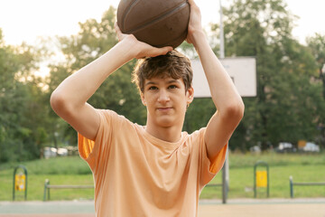 Cute young teenager in t shirt with a ball plays basketball on court. Teenager running in the stadium. Sports, hobby, active lifestyle for boys