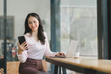 Beautiful asian businesswoman in the cafe, using smartphone and smiling.